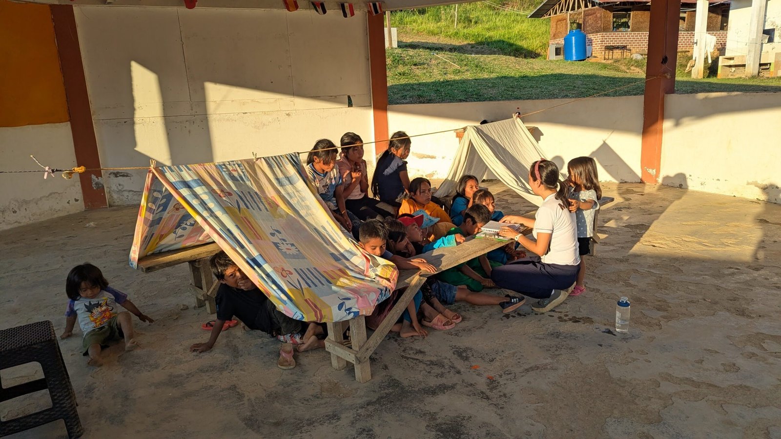 Miriam leyendo un libro con niños nomatsiguenga bajo una carpa de tela